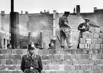 Un policía de Berlín Occidental hace guardia mientras varios albañiles trabajan en el Muro de Berlín.