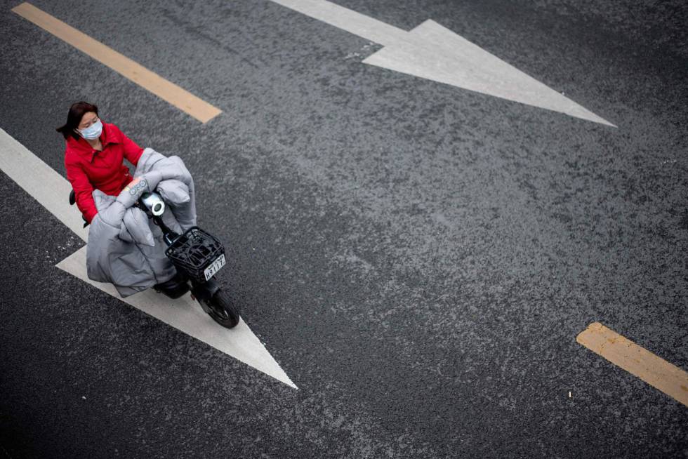 Una mujer protegida por una mascarilla conduce una moto en Wuhan (China).