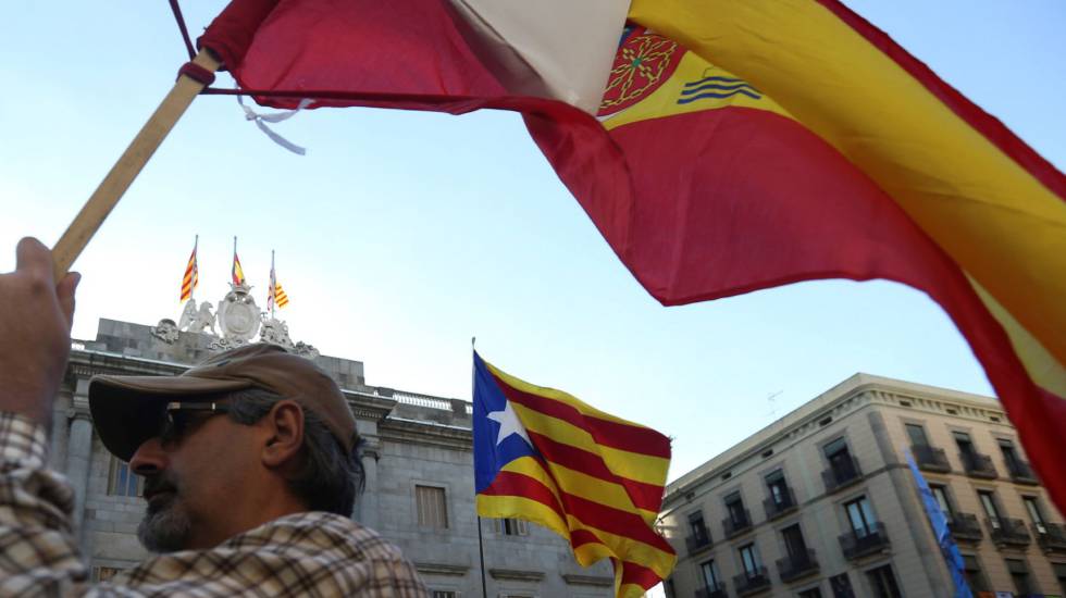 Un hombre porta una bandera de España mientras ondea otra independentista de cataluña al fondo.