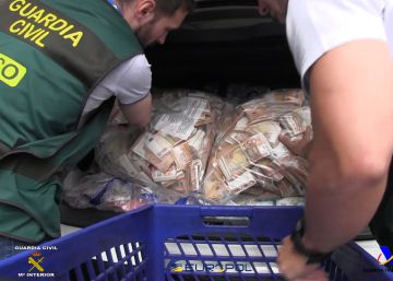 Dos agentes de la Guardia Civil colocan sacos con billetes de 50 euros en un coche.