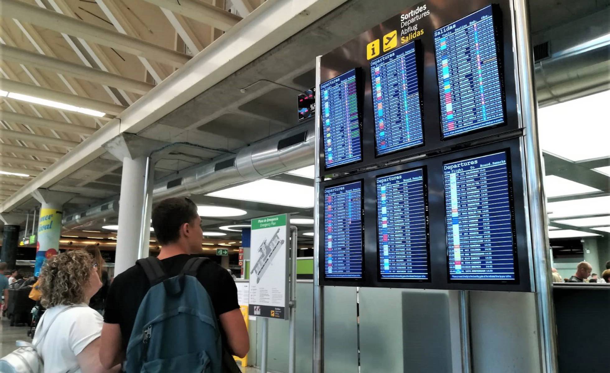 Dos viajeros consultan la información de vuelos en las pantallas del aeropuerto.