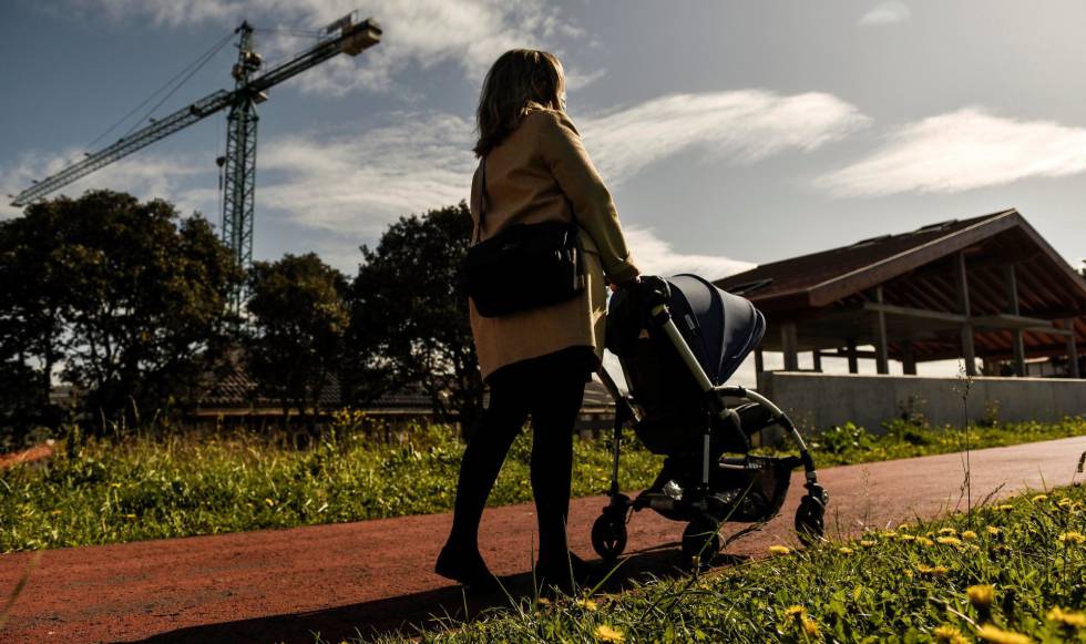 Una mujer pasea junto a su bebé frente a varios edificios en construcción.