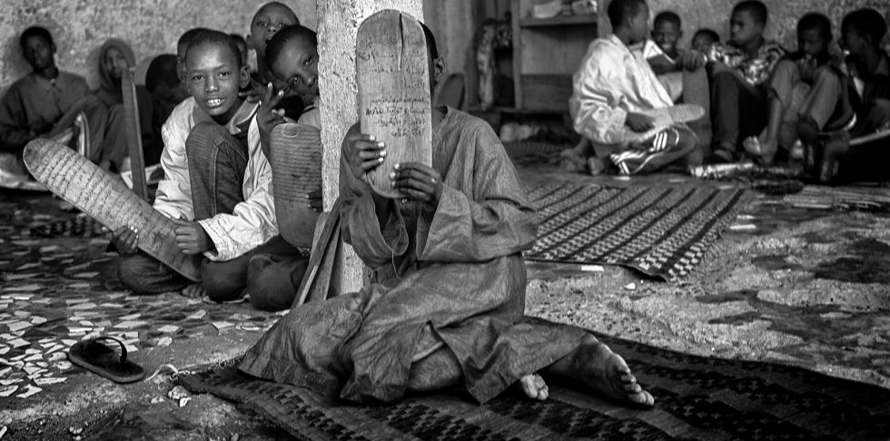 Un niño talibés cubre su cara con una tabla coránica.