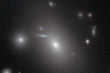 La galaxia el&iacute;ptica NGC 4889, el objeto m&aacute;s brillante en el centro de la imagen, oculta un descomunal agujero negro en su interior