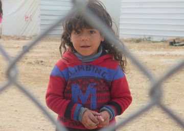Una niña mira a cámara al otro lado de la verja del campo de refugiados de Zaatari, en Jordania.