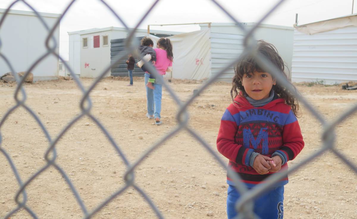Una ni&ntilde;a mira a c&aacute;mara al otro lado de la verja del campo de refugiados de Zaatari, en Jordania.