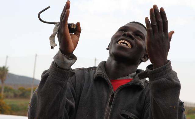 Uno de los inmigrantes invoca al cielo tras lograr saltar la valla. El garfio sirve para trepar por la malla.
