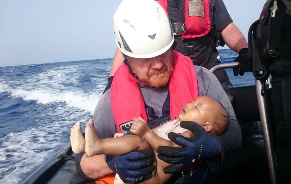 Un miembro de Sea-Watch sostiene a un bebé inmigrante en brazos. Un miembro de Sea-Watch sostiene a un bebé inmigrante en brazos.