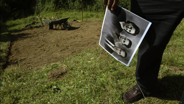 Una mujer sostiene la foto de sus padres junto a una fosa común.