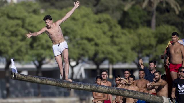 Un participante de la cucaña intenta coger la bandera.