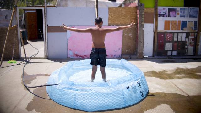 Un ni&ntilde;o se ba&ntilde;a en una piscina hinchable, en el asentamiento chabolista de El Vacie en Sevilla.
