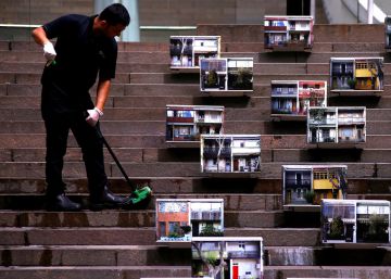 Persona limpiando los escalones de un edificio donde hay colocadas fotografias de terrazas, en el centro de S&iacute;dney (Australia).