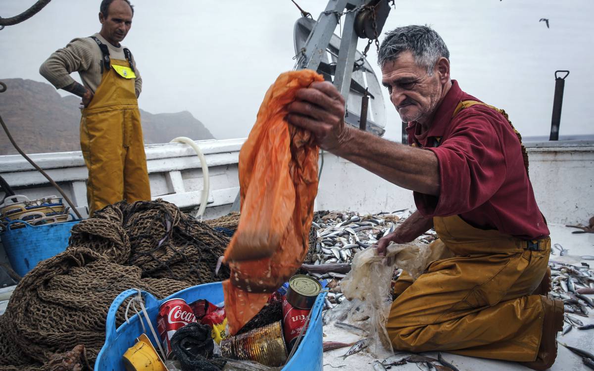 Pescadores separan el plástico de los peces pescados en el arrastre.