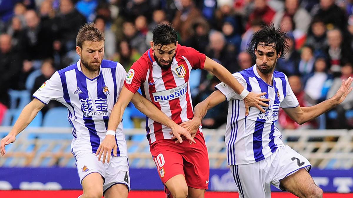 Carrasco (c) del Atlético de Madrid presionado por Asier Illarramendi (i) y Carlos Martínez.