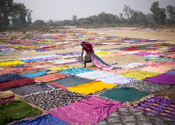 Una mujer recoge pa&ntilde;uelos de colores,antes tendidos, en Agra en India.