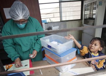 Un ni&ntilde;o con tuberculosis tiende la mano para coger las p&iacute;ldoras de pie junto a una enfermera en un puesto de salud en las afueras de Lima (Per&uacute;)