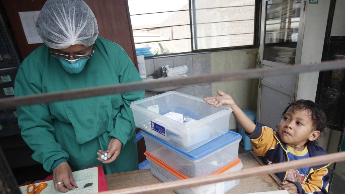 Un niño con tuberculosis tiende la mano para coger las píldoras de pie junto a una enfermera en un puesto de salud en las afueras de Lima (Perú)