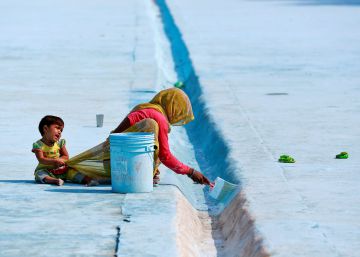 Una mujer pinta el hormig&oacute;n de un estanque mientras su hijo tira de su ropa, en Delhi (India).