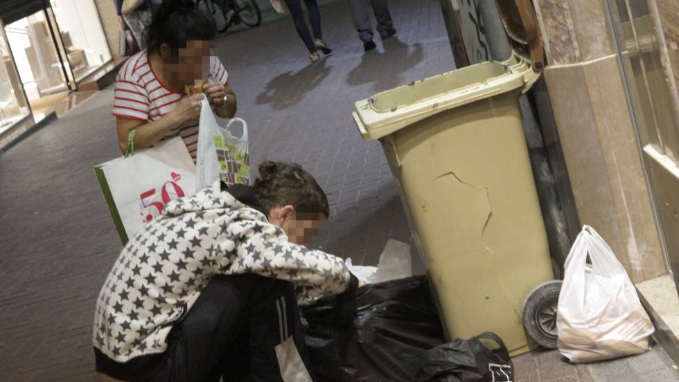 Dos personas buscando comida en unos contenedores de basura.