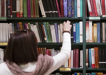 Una mujer coge un libro de una estanter&iacute;a.