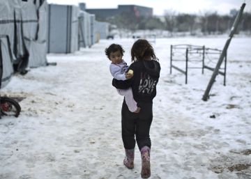 Una ni&ntilde;a siria camina con su hermana en brazos en el campo de Ritsona, en Grecia.