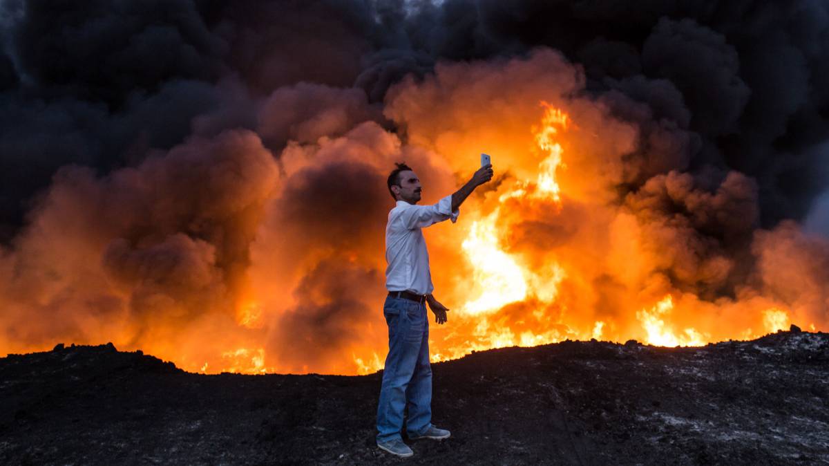 Un hombre se fotograf&iacute;a frente a un fuego, en Qayara (Irak).