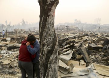 Dos personas se abrazan frente a los escombros de Santa Olga.