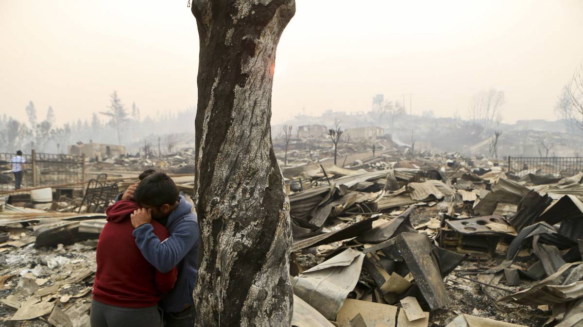 Dos personas se abrazan frente a los escombros de Santa Olga.