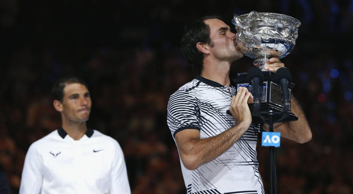 Roger Federer besa el trofeo del Open de Australia ante la mirada de Nadal.