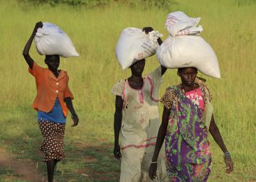 Mujeres sursudanesas regresan a sus casas tras recibir sacos de asistencia alimentaria.