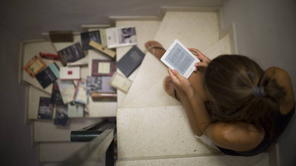 Una joven lee en un libro electrónico junto a varios libros en papel.