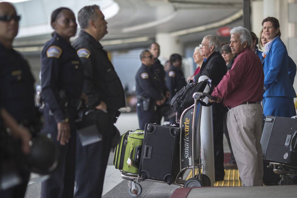Agentes de policía y viajeros en la salida de un aeropuerto.rn
