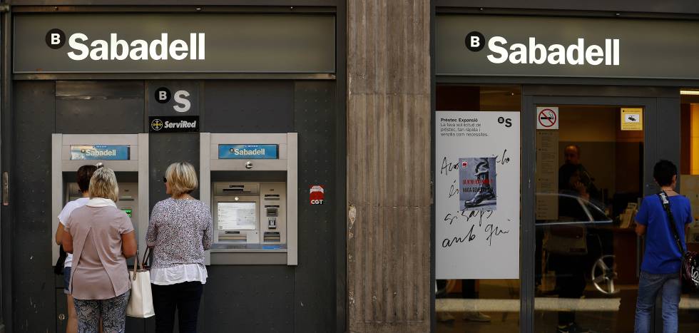 Gente saca dinero en un cajero de una oficina del Sabadell en Barcelona.