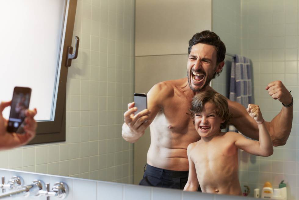 Reflection of father and son flexing muscles while photographing themselves in bathroom
