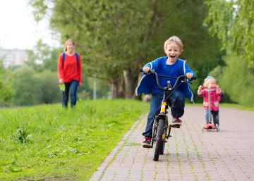Dos niños juegan en un parque con una bicicleta y un patinete.
