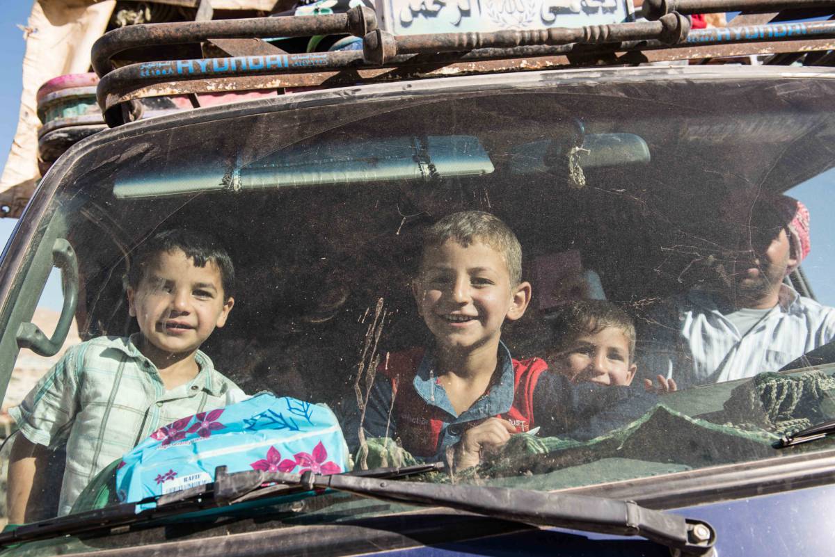 Varios niños sonríen desde un coche del convoy de refugiados que partió de Arsal hacia Siria.