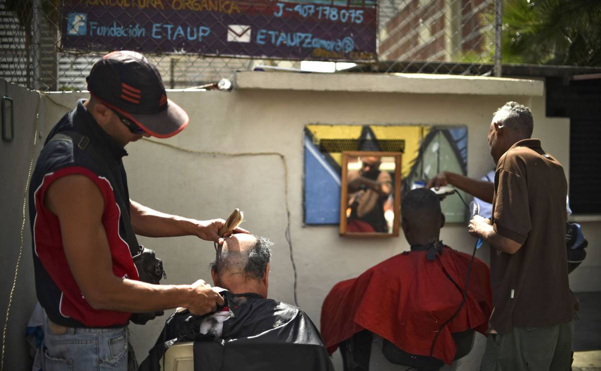 Dos hombres se cortan el cabello en una peluquería improvisada en Caracas.