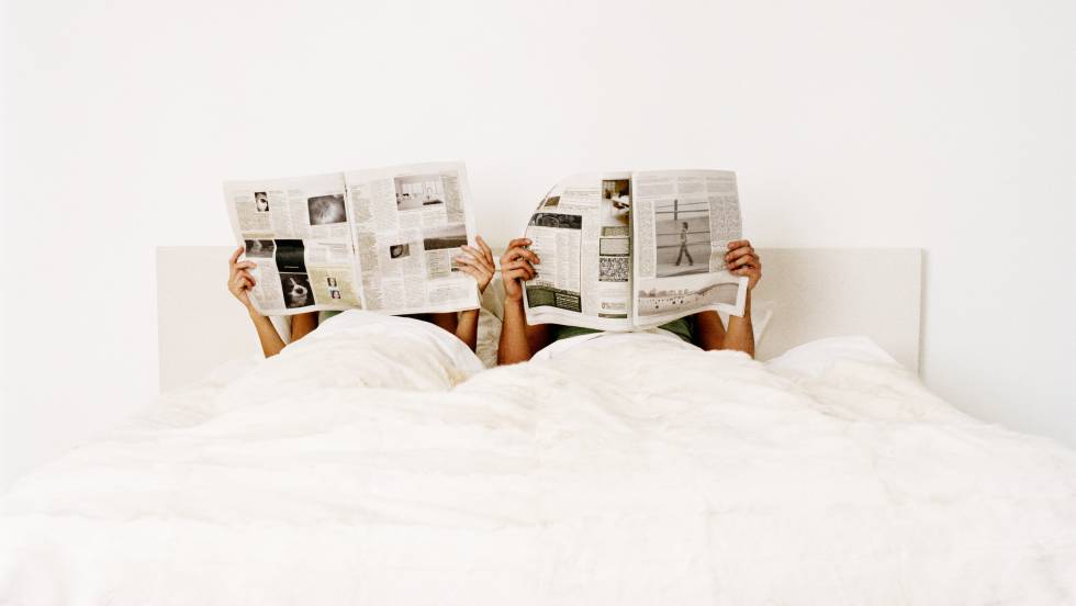 Una pareja en la cama leyendo periódicos.