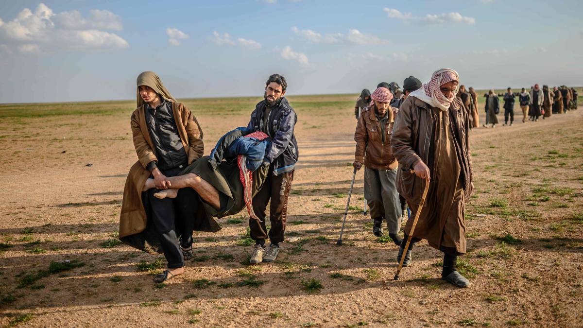 Varios hombres, sospechosos de pertenecer al Estado Islámico, sujetan un herido, mientras avanzan hacia las Fuerzas Democráticas Sirias, lideradas por los kurdos, tras abandonar Baghouz, en la provincia de Deir Ezzor, al norte de Siria.