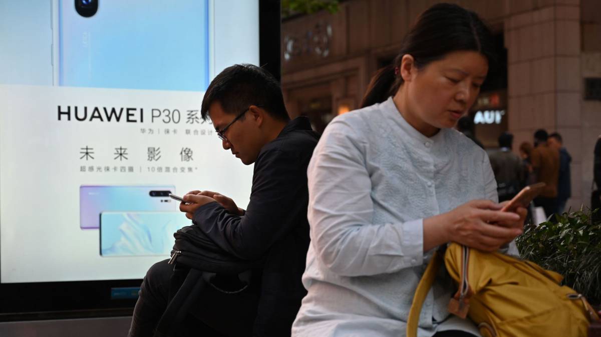 Usuarios de teléfonos junto a un anuncio de Huawei.