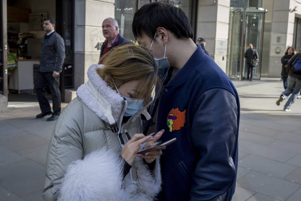 Una pareja asiática hace uso de su teléfono móvil en una calle de Londres durante la crisis del coronavirus.