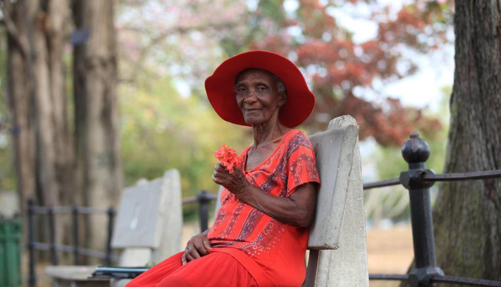 Una mujer mayor ataviada con sombrero disfruta en solitario de un día de sol en el Queen's Park Savannah, el principal parque de Puerto España (Trinidad y Tobago), pese a las restricciones y la orden de quedarse en casa.