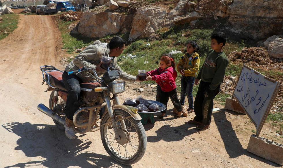 Tayma, de cuatro años, vende licor casero con sus hermanos a un motorista cerca del campamento de desplazados de Bab al-Hawa, en la provincia siria de Idlib, el 26 de abril de 2020.