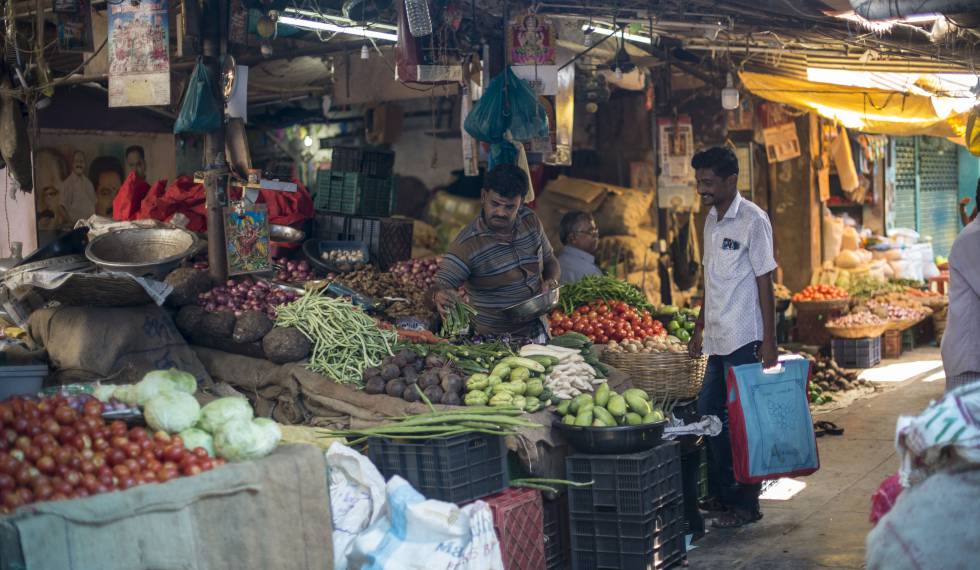 Un hombre con una bolsa de tela para hacer la compra adquiere legumbres en un mercado de Bombay.