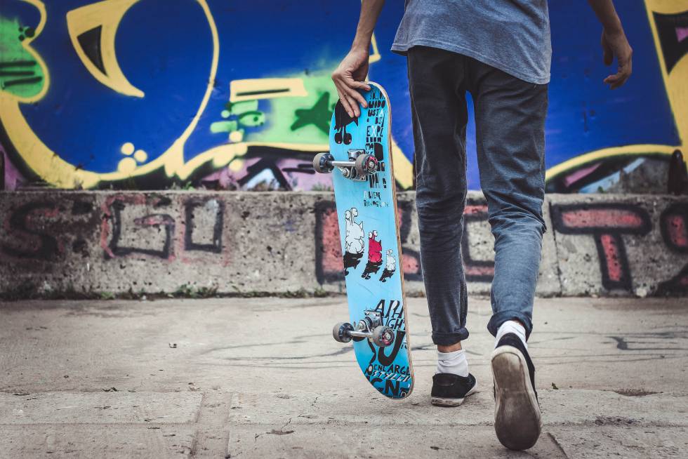 Un adolescente pasea con su monopatín.