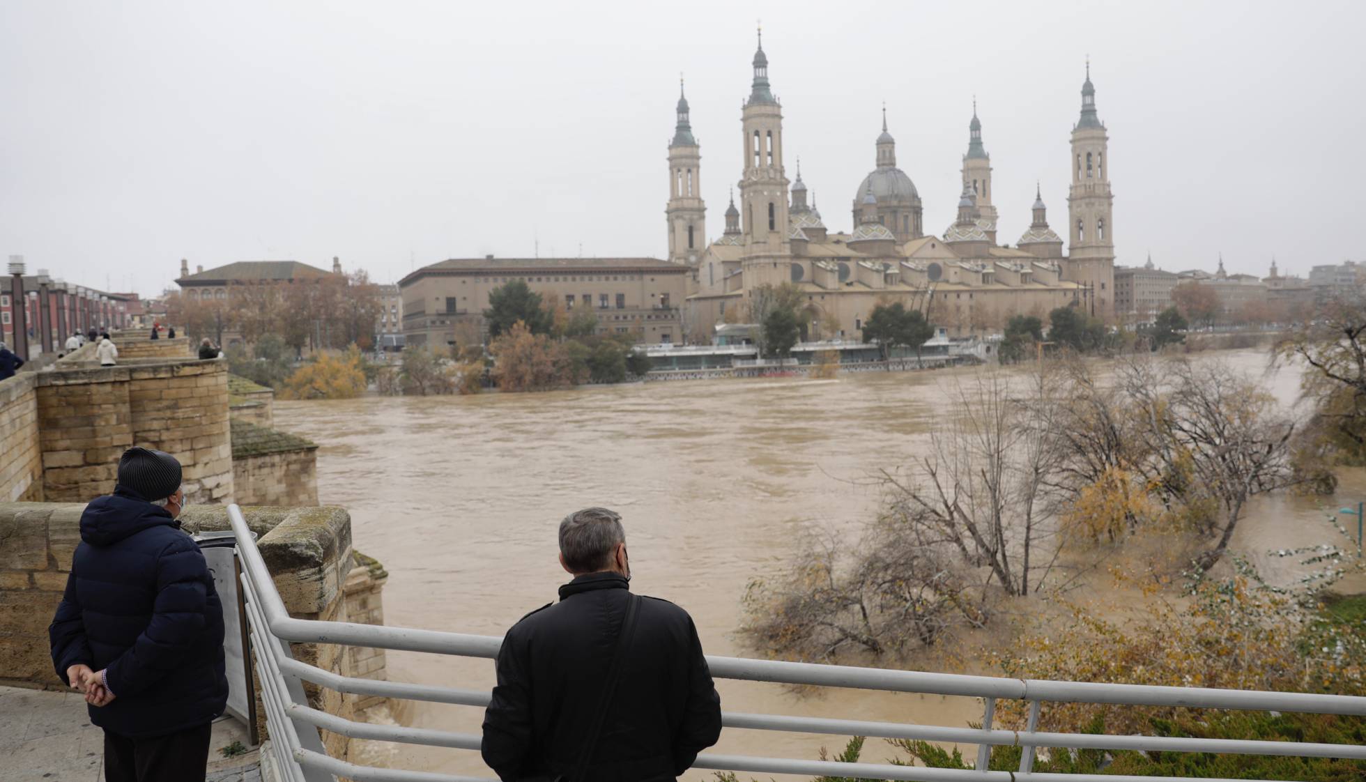 Varios vecinos de Zaragoza observan la crecida del río Ebro, este martes.