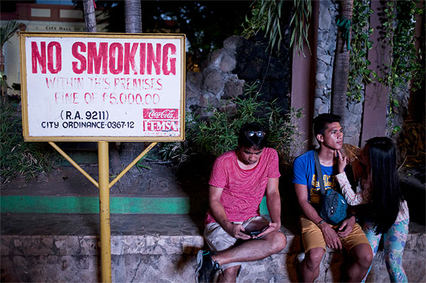 Un grupo de jóvenes descansa en la plaza del ayuntamiento de Davao, junto a una señal que informa de la prohibición de fumar en los espacios públicos bajo castigo de multas para quien infrinja la norma