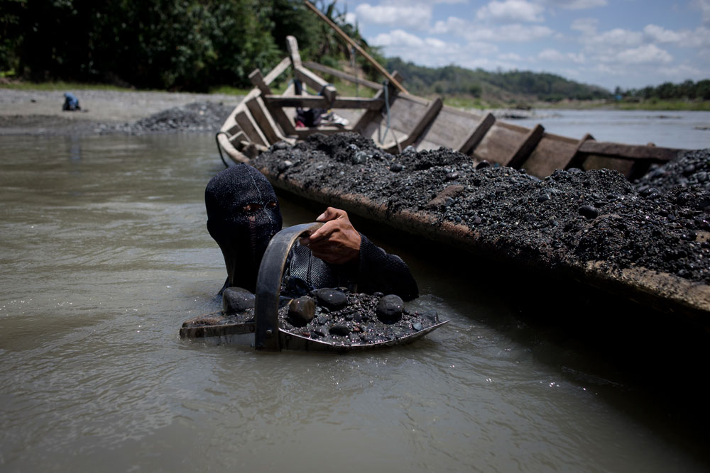 Idan, cubierto por un pasamontañas, recoge a mano piedras y arena del lecho del río Davao para su pequeña cantera artesanal