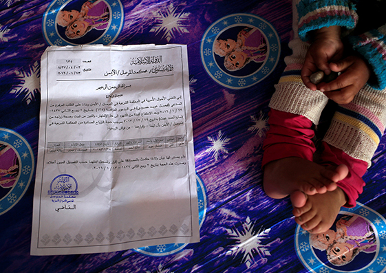 Houda, de dos años, está sentada junto a su certificado de nacimiento emitido por el Estado Islámico, el cual no es reconocido por las autoridades iraquíes. En Khazer, Irak, noviembre de 2016.