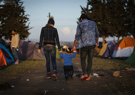 Dos refugiados sirios intentan mantener la normalidad llevando a pasear a su pequeño hijo en el improvisado campo cerca de Idomeni, Grecia en marzo de 2016.